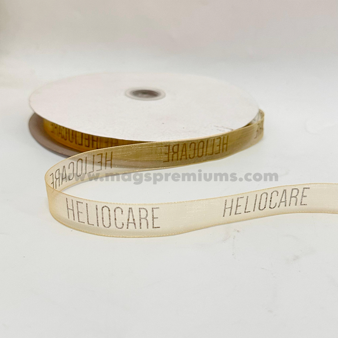 Printed organza ribbon in cream color with repeated HELIOCARE logo branding, supplied on a ribbon roll for gift wrapping, product packaging, event decorations, and corporate branding.